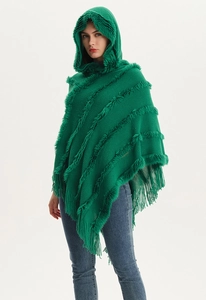 Detail of green hooded knit poncho featuring faux fur trim and long tassel fringe edges