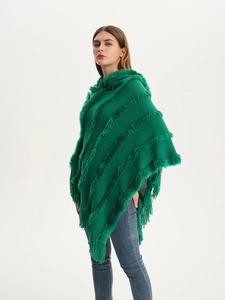 Close-up of green knit poncho with plush faux fur stripes and dense fringed tassels