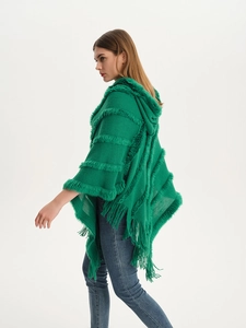 Detail of emerald green knitted poncho showing hooded faux fur trim and long tassels