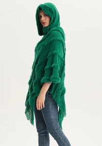 Detail of green hooded knit poncho featuring thick faux fur trim and long fringe tassels