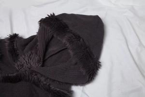 Detailed close-up of dark grey knitted hooded shawl with thick faux fur trim on white fabric