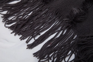 Close-up of charcoal gray knit shawl featuring long tassel fringe details and texture
