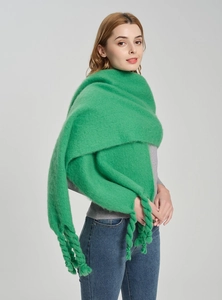 Detail of bright green shawl featuring thick braided tassels and cozy boucle yarn texture