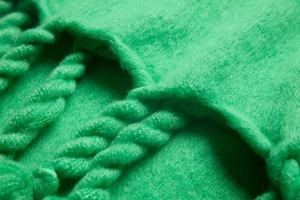 Macro detail of plush green fabric scarf showing thick braided tassels and soft texture