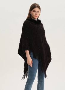 Detail view of dark knit poncho featuring sequins, faux fur collar, and fringe tassels