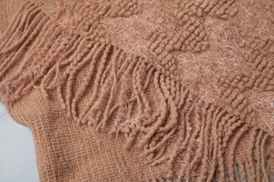 Close-up of camel knit cape with fringe details and subtle sequin accents for texture