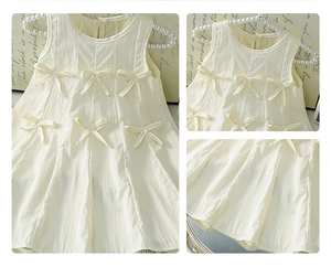 Detail view of girls sleeveless cream dress featuring decorative bows and vertical pleats