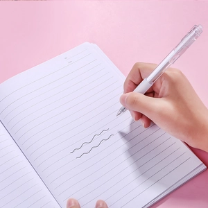 Transparent retractable gel pen with black ink shown writing on a notebook on a pink desk