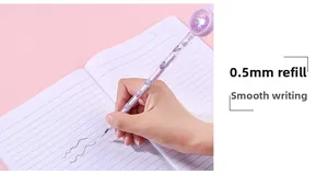 Gros plan d'une main écrivant avec un stylo pailleté papillon violet sur un carnet