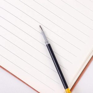 Macro shot of 0.5mm black ink gel pen refill with needle tip on lined notebook
