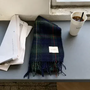 Gros plan d'une écharpe à carreaux vert foncé avec des franges et une étiquette tissée