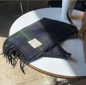 Gros plan d'une écharpe à carreaux rétro avec pompons et étiquette tissée sur table
