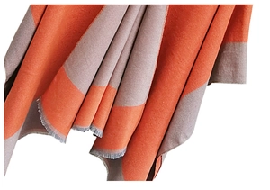 Detail of knit shawl featuring orange and grey color block with raw fringe edges