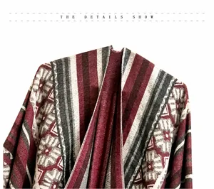 Detalle del patrón jacquard geométrico en un poncho de punto burdeos con flecos