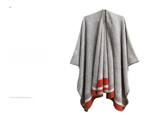 Detail of grey knit poncho featuring vibrant orange and blue stripes and fine stitching
