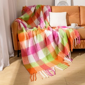 Detail of colorful plaid knitted blanket with soft tassels on an orange leather sofa
