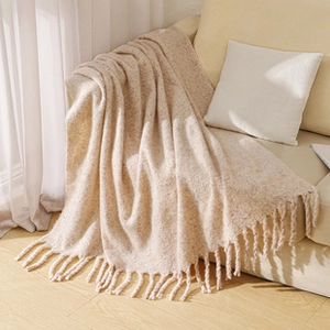 Close-up of beige knit blanket texture and handmade tassel edge on a fabric sofa
