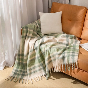 Close-up of green and white checkered knit throw blanket with decorative fringe tassels