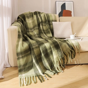 Detail of green and white plaid throw blanket with tassels on a cozy living room sofa