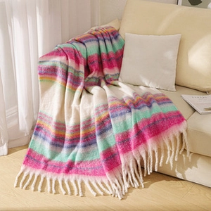 Close-up of knit rainbow striped blanket with decorative long tassels on a sofa