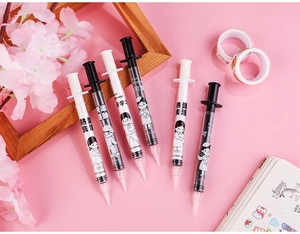Detail of creative syringe-shaped pens with motivational quotes on a soft pink desk setup
