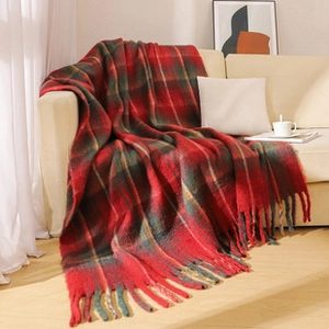 Close-up of red and green plaid throw blanket with soft fringe detail on beige sofa