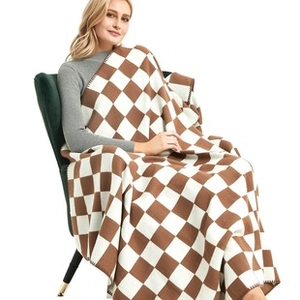 Detail of a brown and white checkered knit throw blanket with fringe and soft texture