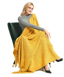 Detail of yellow knit throw blanket with diamond pattern and long fringed tassels