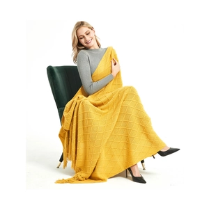 Detail of yellow knit throw blanket with diamond patterns and decorative fringe tassels