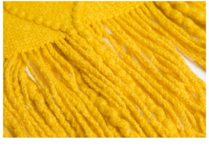 Macro detail of soft yellow knitted blanket featuring long tassels and woven texture