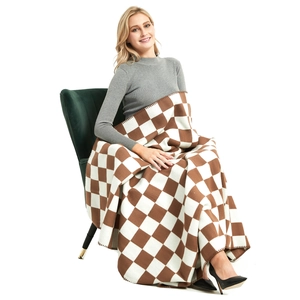 Brown and white checkerboard knit throw blanket draped over a woman on a green velvet chair