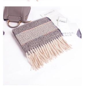 Detail of gray knitted scarf with stripes and thick tassels next to a gray handbag