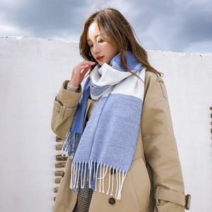 Détail d'une écharpe à carreaux bleus et blancs avec franges sur un manteau beige