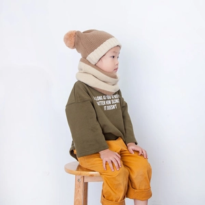 Close-up of children's thick knitted hat and scarf set with pom-pom and contrast colors