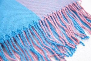 Gros plan d'une écharpe à carreaux bleu et rose avec texture tissée douce et des franges