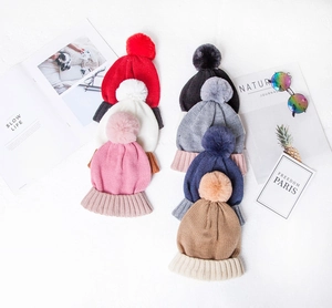 Detailed view of knitted pom-pom beanies in various colors with wide ribbed cuffs