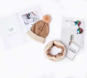 Flat lay of color-block knit hat and neck warmer set with fluffy pompom detail