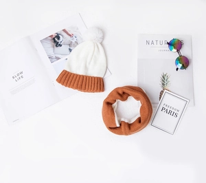 Flat lay of a white and orange knit winter hat with pom-pom and matching neck warmer
