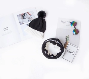 Flat lay of black and white color-block knitted hat and scarf set with pom-pom detail