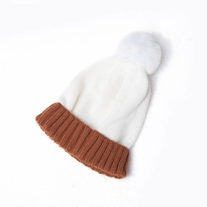 Detail of color-block knit beanie with white faux fur pompom and ribbed cuff
