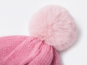 Close-up of pink knit hat featuring soft textured weave and fluffy pom-pom detail