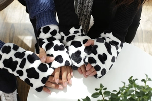 Primer plano de guantes gruesos de felpa sin dedos con estampado de vaca en blanco y negro