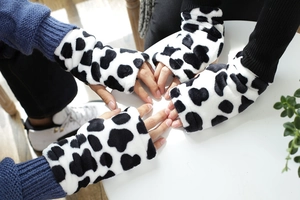 Detalle de guantes de peluche sin dedos con estampado de vaca y textura suave de forro
