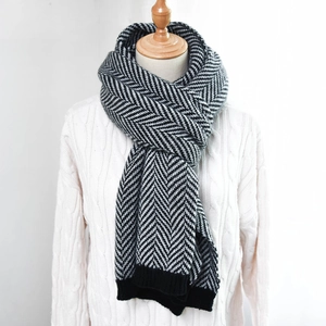 Detail of herringbone knit scarf with ribbed edge worn over a white cable knit sweater