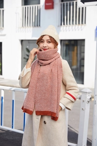 Detail of red herringbone knit scarf with fringe and a cream ribbed beanie hat