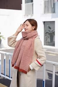 Detail of winter herringbone knit scarf in rust red and beige shown with a coat