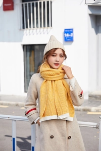 Outdoor shot of a woman in a beige wool coat wearing a yellow knitted chevron scarf