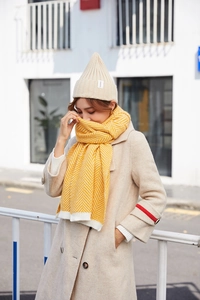 Detailed view of yellow herringbone knitted scarf with a matching beige ribbed beanie hat