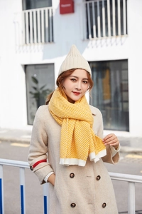 Detail of yellow chevron knit scarf with white trim on a model in a wool coat