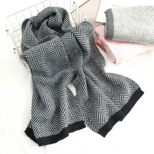 Detail of herringbone knit scarf with ribbed edges hanging on a white metal basket